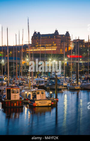 Scarborough Harbour, vista al tramonto della zona del porto e oltre, il Grand Hotel situato sulla skyline di Scarborough, North Yorkshire. Foto Stock