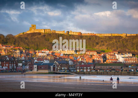 Scarborough Beach, vista fuori stagione di South Bay Beach a Scarborough con il castello sopra la città illuminata da un tramonto, Inghilterra, Regno Unito Foto Stock