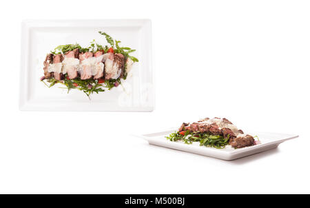 Carne di manzo caldo rib-eye carne succosa bistecca, mezzo raro, tagliata a fette sul piatto bianco con insalata di spinaci e aglio, close-up, vista da sopra. Foto Stock