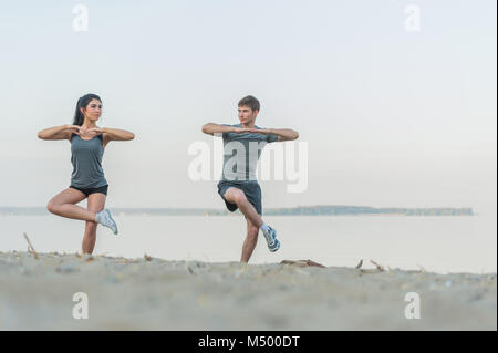 Fitness, sport, amicizia e il concetto di stile di vita - sorridente giovane facendo stretching esercizi yoga sulla spiaggia di mattina Foto Stock