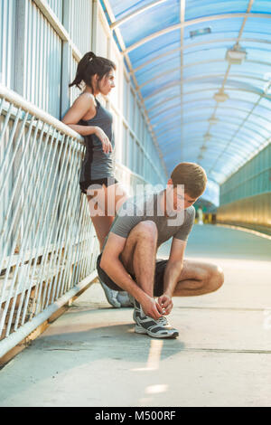 Ottenere pronto per fare jogging. Vista frontale del giovane uomo e donna lacci delle scarpe di legatura e rilassante mentre essendo all'aperto Foto Stock