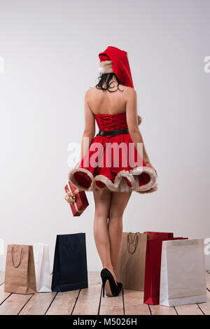 Donna shopping per i regali di Natale. Giovane ragazza caucasica da dietro con le borse della spesa indossando Santa Claus dress e hat Foto Stock