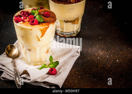 Tre porzionato vetro con dessert italiano Tiramisù con la menta e lamponi, scuro su sfondo arrugginito. Spazio di copia Foto Stock