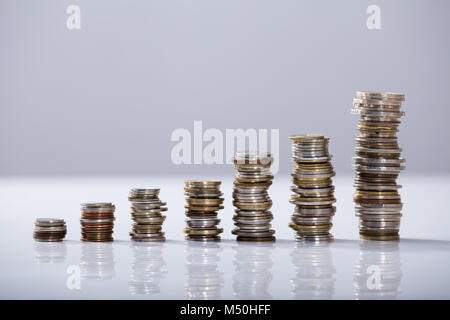 Aumentare pila di monete sul banco riflettente su sfondo bianco Foto Stock
