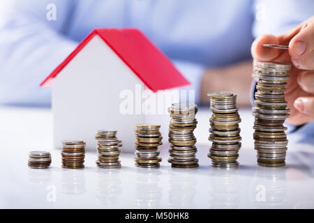 Imprenditore posizionando il gettone sulla sommità della pila di monete di fronte a casa Foto Stock