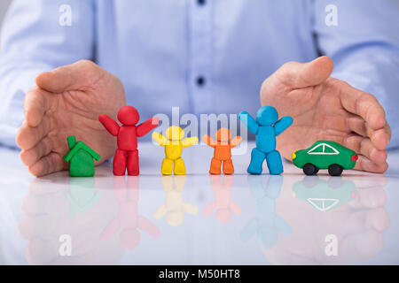 Close-up di mano d'uomo proteggendo la casa, auto e colorata famiglia composta di argilla Foto Stock