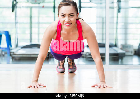 Sorridente giovane donna facendo spinta in su in palestra Foto Stock