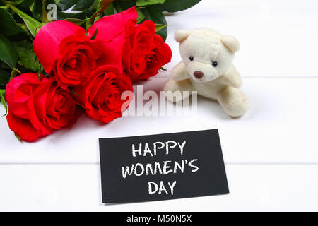 Felice Festa della donna. Il 8 marzo. Rose, Teddy bear e lavagna su un bianco tavolo in legno Foto Stock