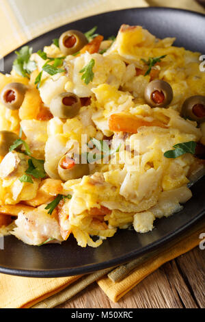 Bacalhau Bass - fried shredded merluzzi salati con patatine fritte, cipolle e uova su una piastra di close-up verticale. Foto Stock