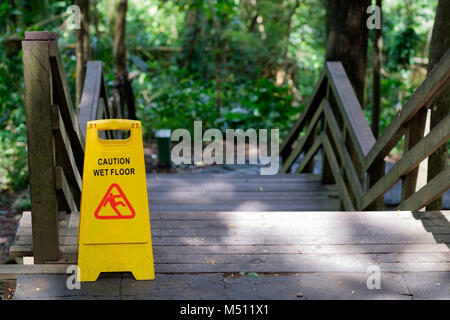 Spia gialla di Attenzione scivoloso pavimento bagnato segno all'aperto vicino a scala in legno Foto Stock