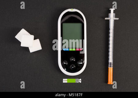 Siringa da insulina glucometro e zucchero bianco i cubi su sfondo nero come diabet e concetto di ipoglicemia Foto Stock