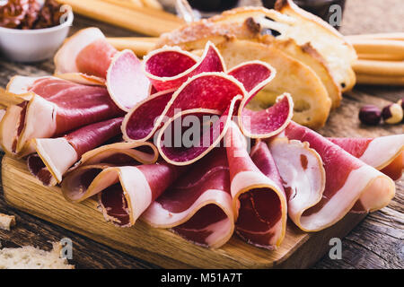 Antipasto piatto con carne affumicata servita con crostini di pane e bastoni. Il cibo italiano, prosciutto, salami e pomodori secchi su legno cinghiale di taglio Foto Stock