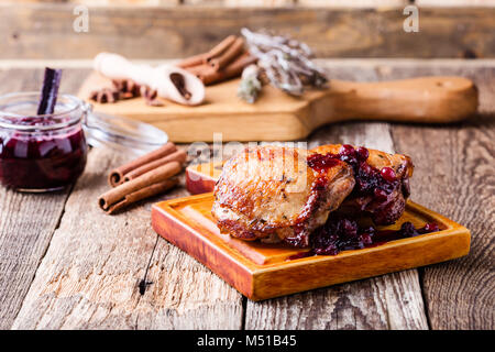 Pollo arrosto gambe sul bordo di taglio servito con salsa di mirtilli su tavola in legno rustico Foto Stock