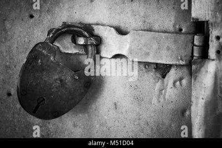 Vecchia serratura arrugginita appeso sulla porta di metallo. Close-up foto in bianco e nero Foto Stock