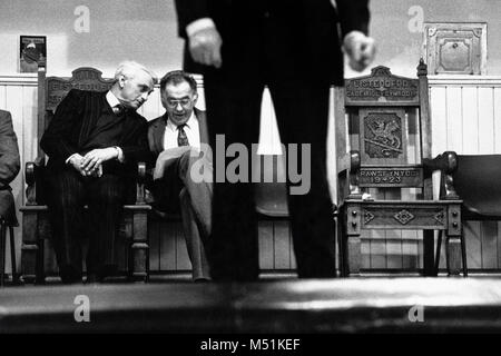 L'uomo prendendo parte al canto solista concorrenza sul palco mentre i membri del comitato chat sul retro dello stadio a piccole eisteddfod nel village hall Trawsfynydd Gwynedd Wales UK Foto Stock