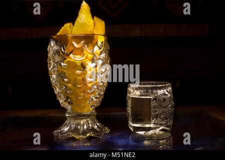 Mezcal messicano in un bicchiere accanto alla tazza di cristallo con fette di arance Foto Stock