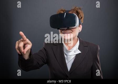 Senior Business lady indossando occhiali vr e puntando su sfondo nero Foto Stock