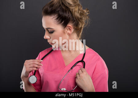 Close-up di bella giovane medico disponendo il suo stetoscopio su sfondo nero Foto Stock