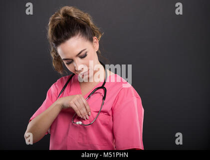 Ritratto di giovane e bella medico disponendo la sua scrub su sfondo nero con copyspace area pubblicitaria Foto Stock