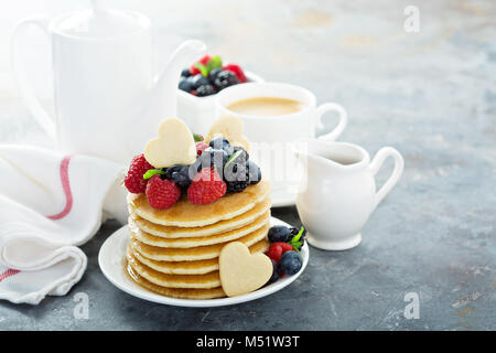 Pila di latticello con frittelle a forma di cuore i cookie, frutti di bosco freschi e sciroppo d'acero per il giorno di San Valentino la prima colazione Foto Stock