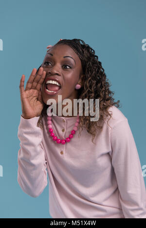 Giovane donna africana gridare e urlare usando le sue mani come un tubo, studio shoot isolato su blu Foto Stock