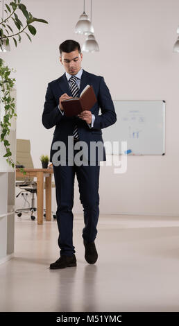 Ritratto di un imprenditore di occupato a prendere appunti e scrivere qualcosa nella sua agenda elettronica presso il suo ufficio Foto Stock