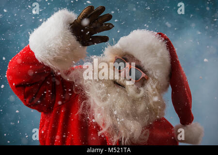 Santa Claus indossando occhiali da sole danza all'aperto presso il Polo Nord in nevicata. Egli sta celebrando il Natale dopo un duro lavoro Foto Stock