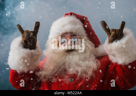 Santa Claus indossando occhiali da sole danza all'aperto presso il Polo Nord in nevicata. Egli sta celebrando il Natale dopo un duro lavoro Foto Stock