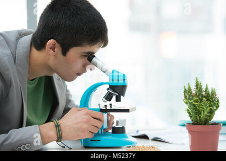 Gli studenti delle scuole superiori. Giovane maschio bello studente guardando attraverso il microscopio campione biologico nella classe di scienze Foto Stock