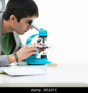 Gli studenti delle scuole superiori. Bel giovane studente maschio del peering attraverso il microscopio nella scienza in aula. Un sacco di copyspace Foto Stock