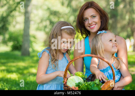 Madre di due figlie nel parco la preparazione per picnic di alimenti biologici Foto Stock