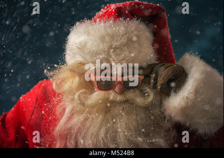 Santa Claus indossando occhiali da sole danza all'aperto presso il Polo Nord in nevicata. Egli sta celebrando il Natale dopo un duro lavoro Foto Stock