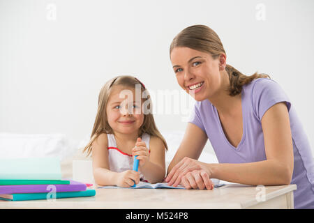 Madre e figlia a casa. La mamma insegna bambina a disegnare e scrivere Foto Stock