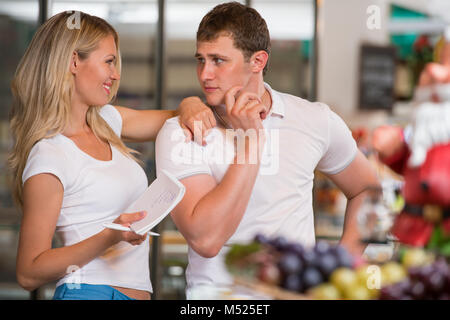 Immagine della coppia positiva la scelta di prodotti in un supermercato con la lista delle cose da comprare Foto Stock