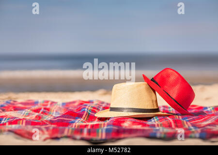 Il bianco e il rosso di cappelli di paglia sul manto colorato sulla spiaggia Foto Stock