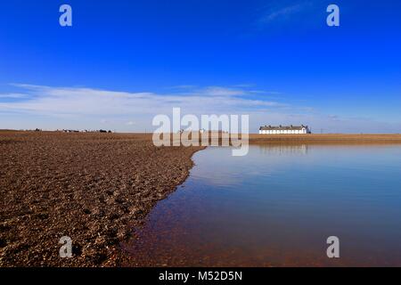 Cottage bianco, una laguna blu e una banca di ciottoli su un luminoso inverno mattina a Shingle Street, Suffolk, Regno Unito. Foto Stock