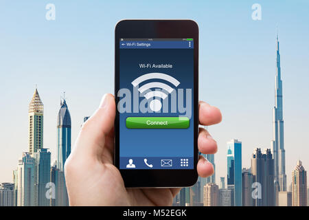 Close-up di mano azienda Smart Phone con Wi-fi la disponibilità sullo schermo contro la costruzione di grattacieli Foto Stock