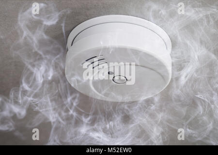 Close-up di un rilevatore di fumo sul soffitto, circondato dal fumo Foto Stock