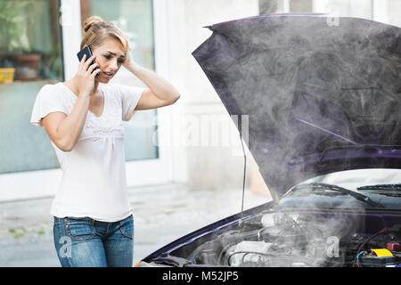 Giovane donna parlando al telefono mobile di fronte Smokey auto motore Foto Stock