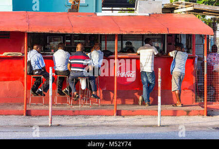 Bridgetown, Barbados - Gennaio 31th, 2018: la gente seduta in un rosso street bar con la Coca Cola segno situato presso il terminal degli autobus di Bridgetown. Foto Stock