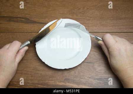 Bianco vuoto cina piastra con mani pewter coltello e forchetta su assi di legno con copia spazio. Foto Stock