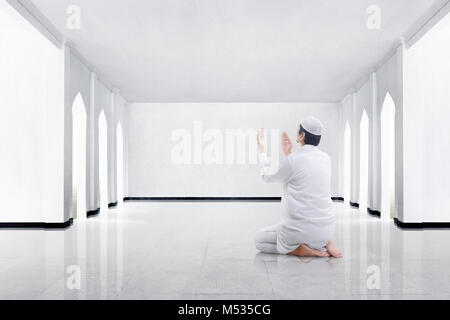 Vista posteriore dei musulmani asiatici uomo inginocchiarsi e pregare Dio nella moschea Foto Stock