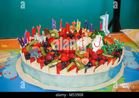 Una prima torta di compleanno decorata con frutta estiva, toy animali e candeline di compleanno. Foto Stock