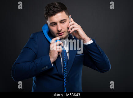 Imprenditore occupato al lavoro parlando su due telefoni come concetto di multitasking Foto Stock