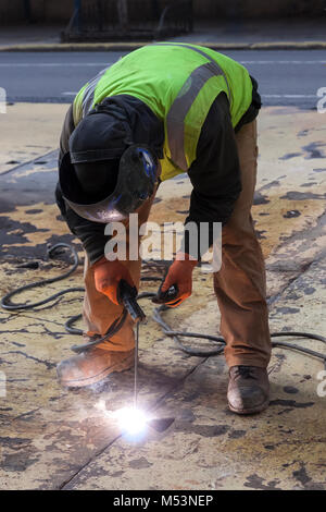 Un lavoratore la saldatura di una piastra di acciaio su un New York City street. Foto Stock