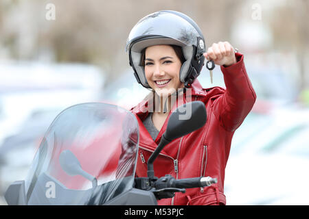 Felice di motociclisti che mostra i tasti seduto sulla sua nuova moto all'aperto sulla strada Foto Stock