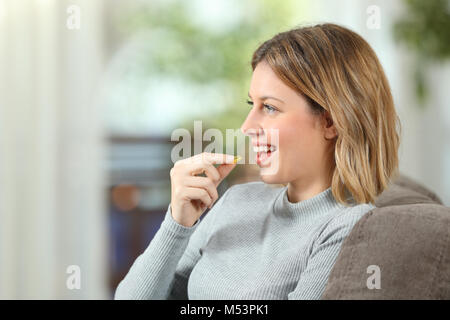 Profilo di una donna felice di prendere una pillola di vitamina seduta su un divano nel salotto di casa Foto Stock