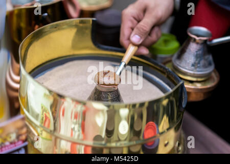 Close-up delle mani dell'uomo facendo tradizionale caffè turco con schiuma in rame turk sulla calda sabbia. La preparazione del caffè concept Foto Stock
