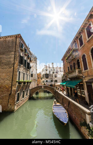 La bella città di veneziani di canal percorsi e giri in gondola, sun flair nell'angolo con vecchi edifici del comune di fronte. Foto Stock