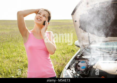 Giovane donna parlando al telefono mobile di fronte Smokey auto motore Foto Stock